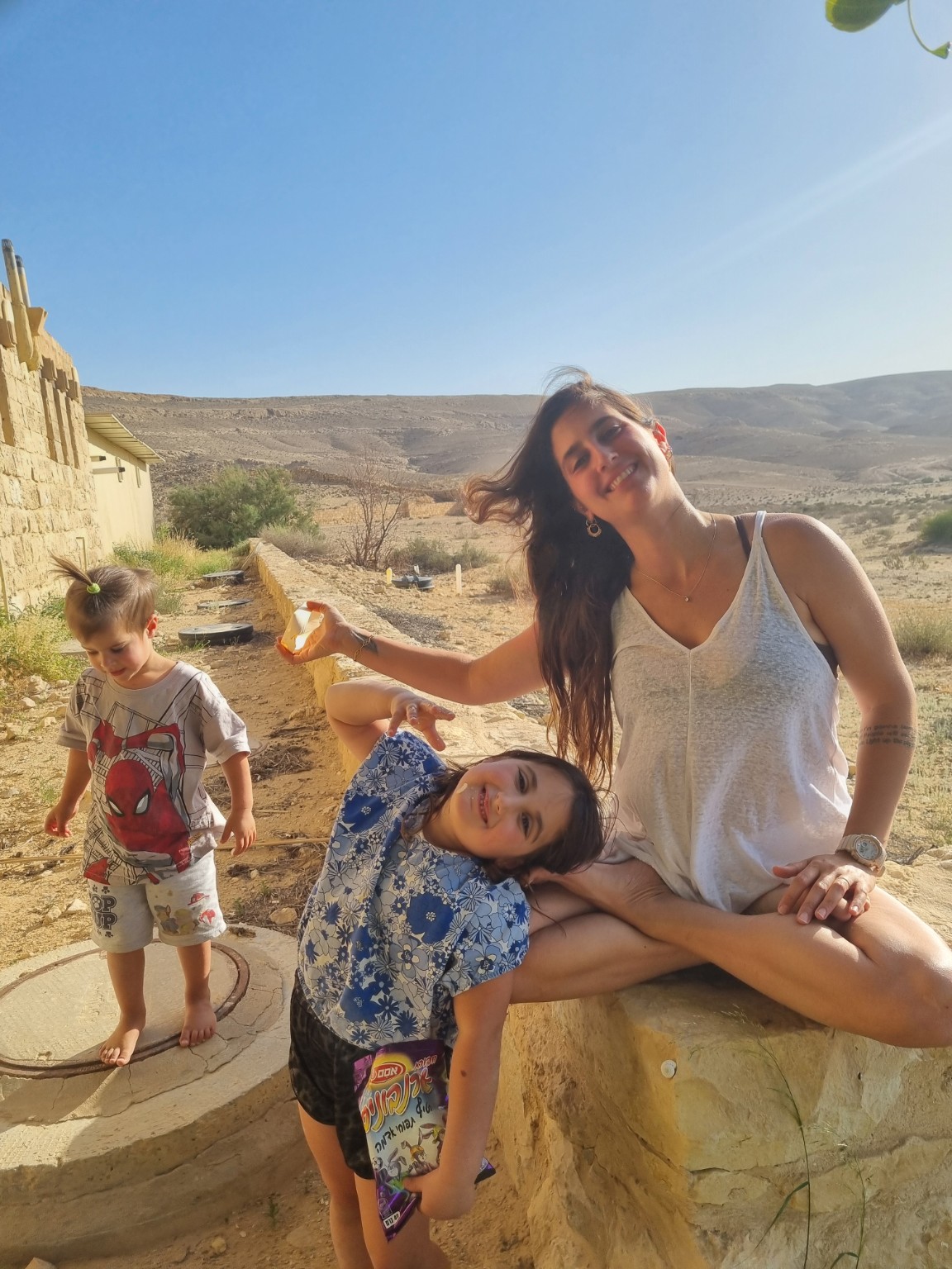 מאיה מחייכת בחוץ לצד שני ילדים