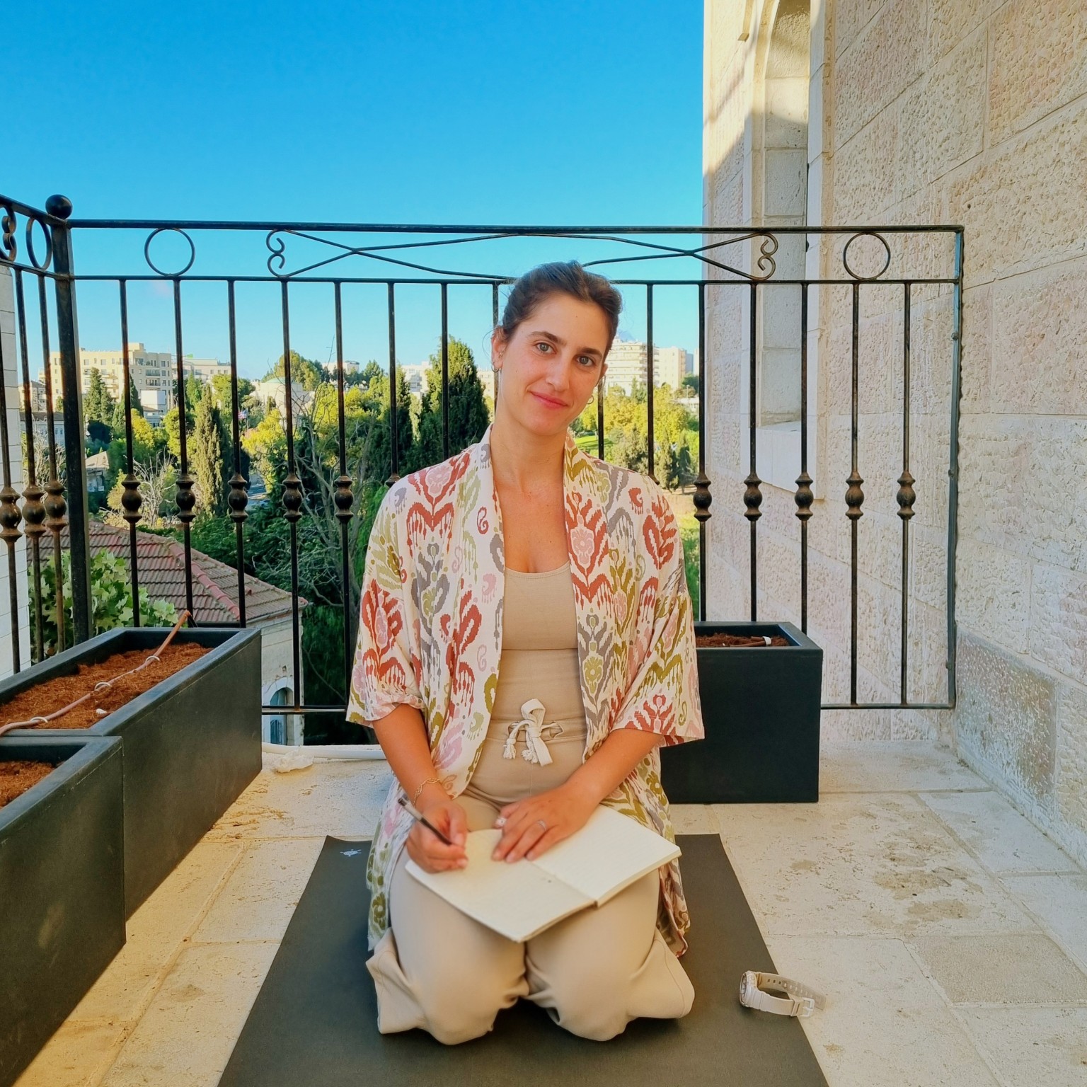 מאיה יושבת עם מחברת פתוחה במרפסת, באור יום